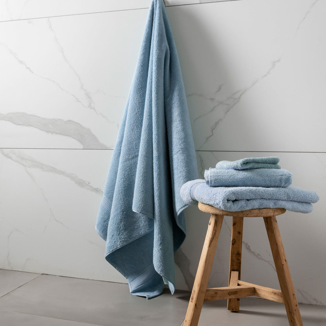 Colibri-imperial-Coronet-blue-1 stool against a marble-tiled wall in a bathroom setting.