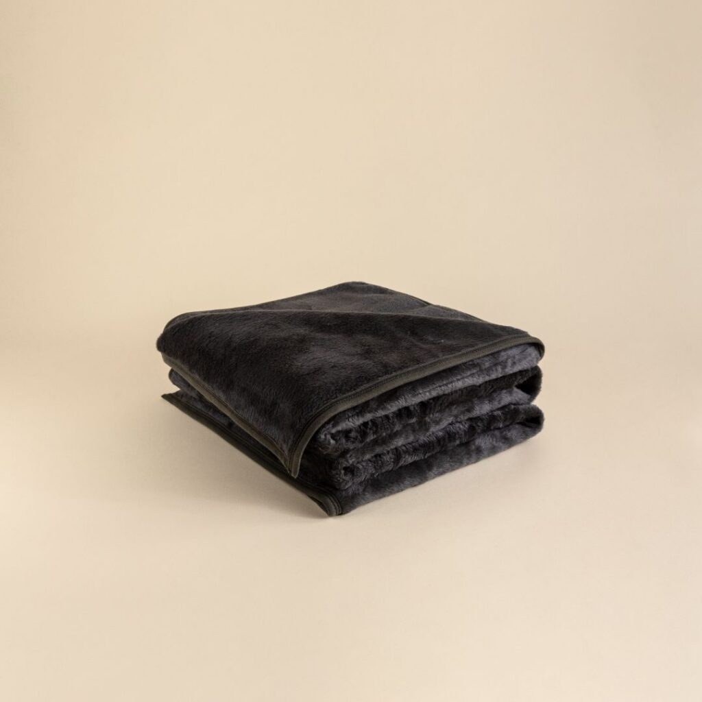 A folded dark blue blanket on a beige background, likely made of cotton and polyester.