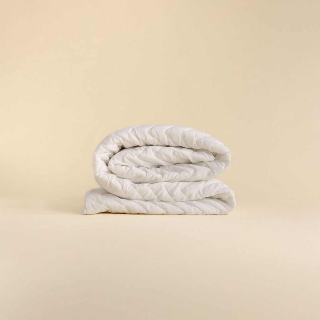 Folded white quilted hollow fibre mattress protector on a beige background