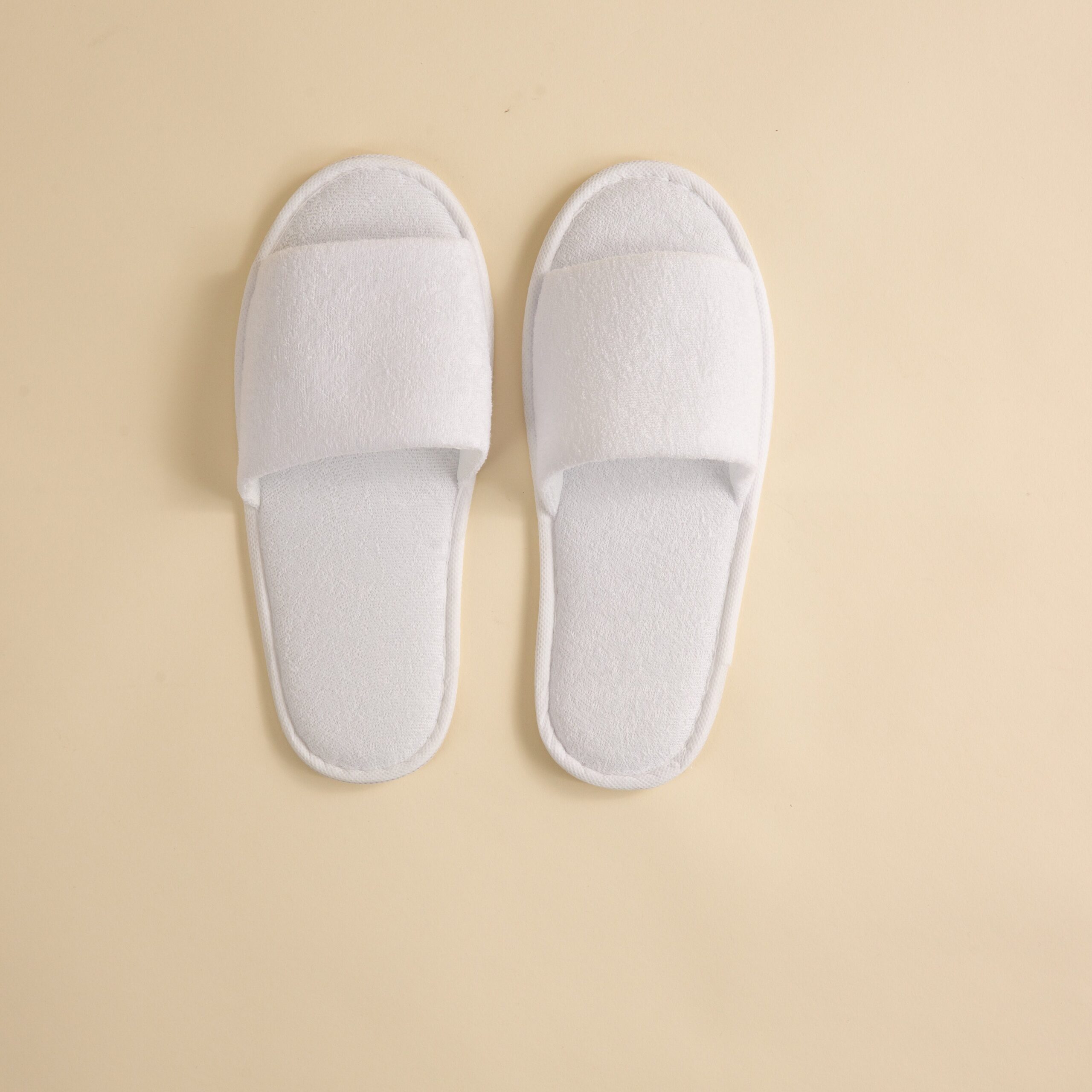 FineDetailsDay2-094 A pair of white towelling open-toe slippers placed on a neutral background.