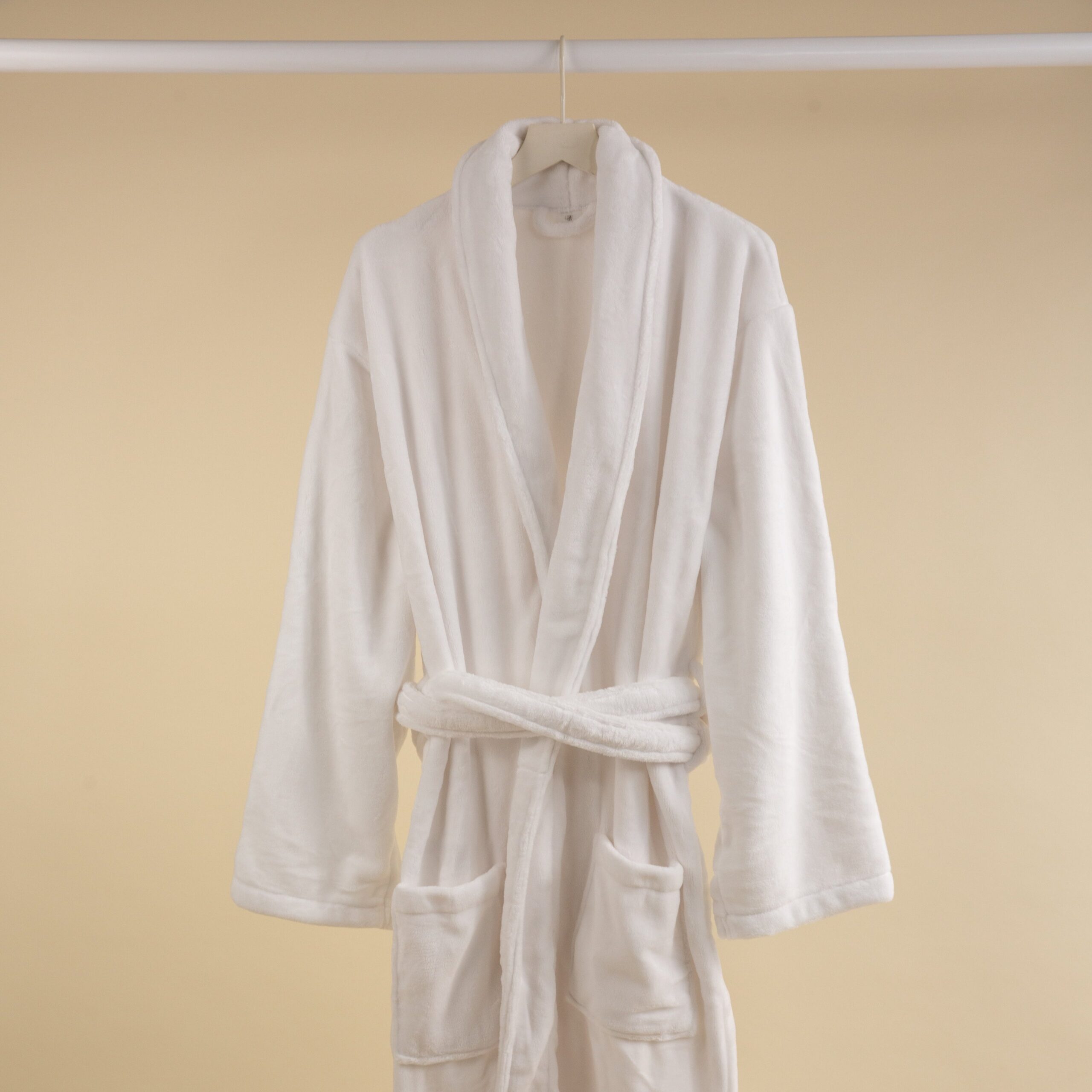 FineDetailsDay2-173 A white coral fleece bathrobe hanging on a rod against a beige background.