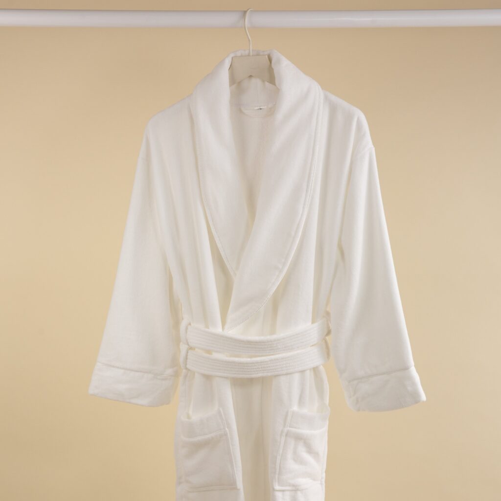 A white velour towelling bathrobe hanging against a beige background.