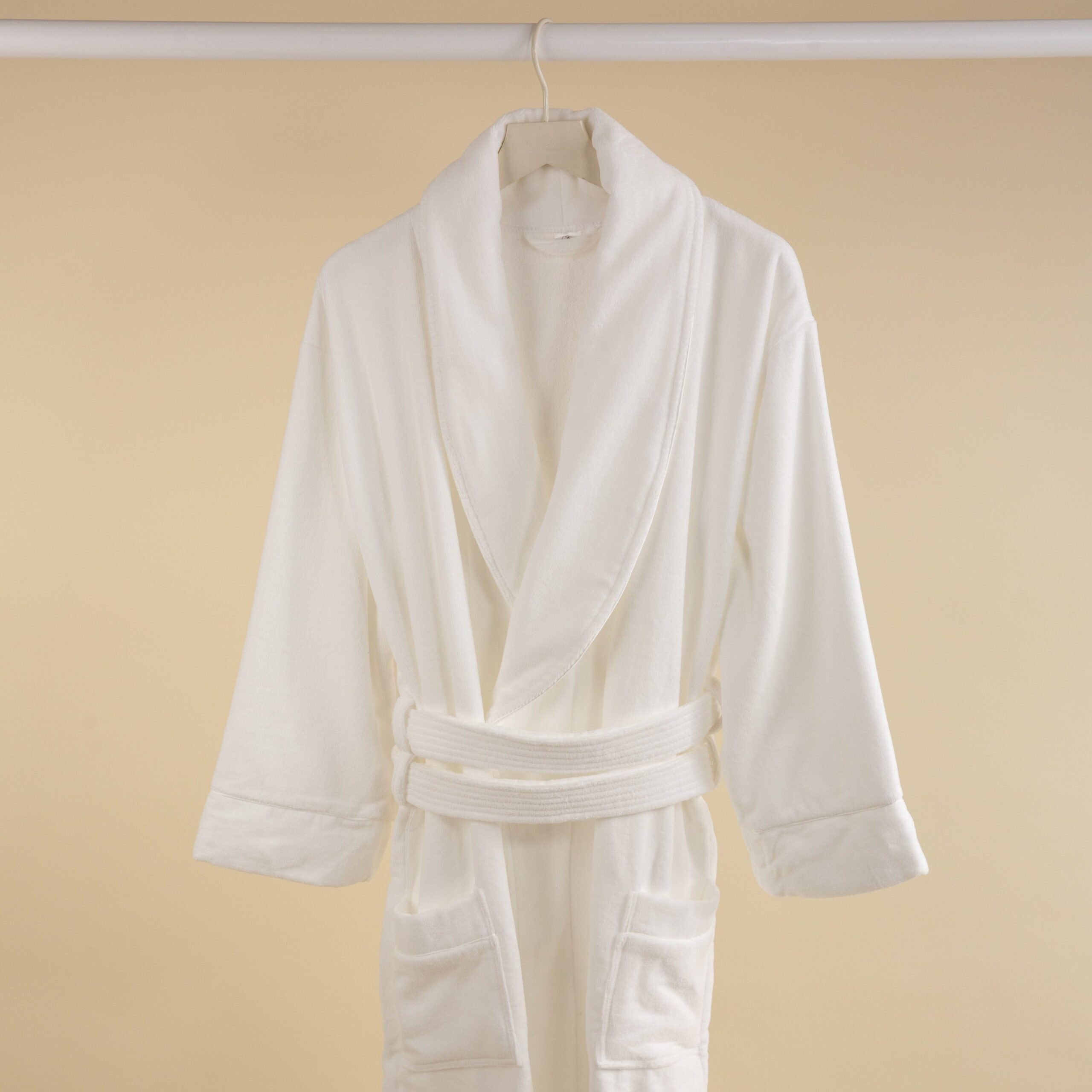 FineDetailsDay2-180 A white velour towelling bathrobe hanging against a beige background.