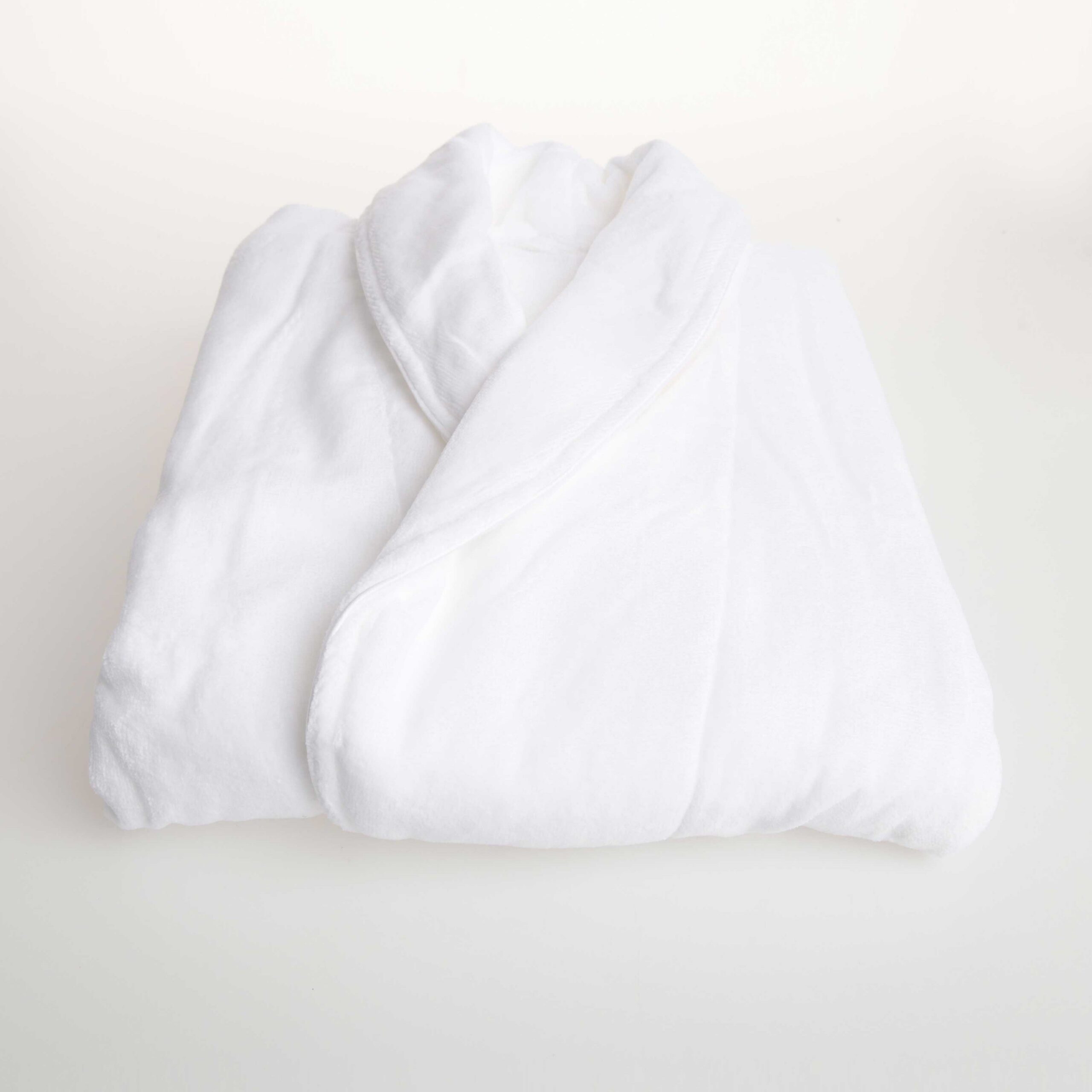 Velour-Robe-Detail White bathrobe folded neatly on a light beige surface