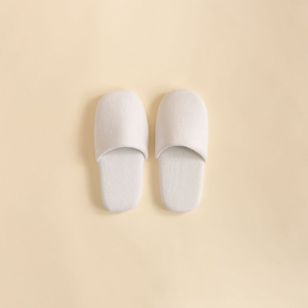 A pair of white velour closed-toe slippers placed on a light-colored surface.